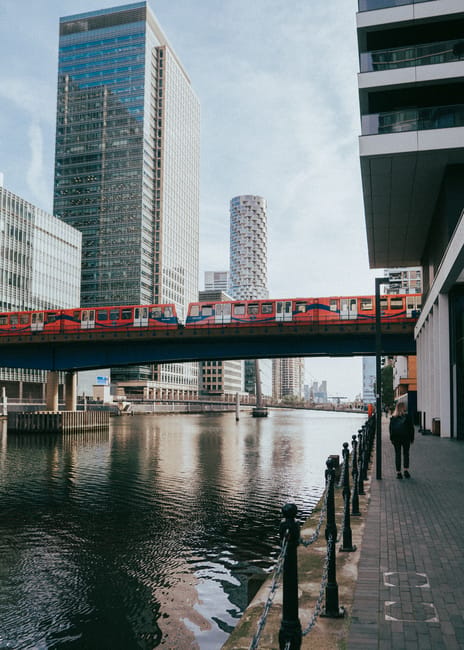 A panoramic view of a modern city skyline with numerous high-rise buildings of varying heights, featuring glass facades and contemporary architectural designs, set against a bright blue sky with some 