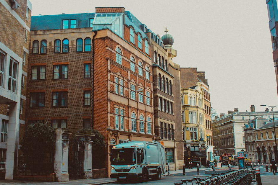 A narrow urban alleyway flanked by tall brick buildings on both sides, with weathered red and brown bricks featuring white mortar joints. The alley's asphalt surface displays yellow double lines runni